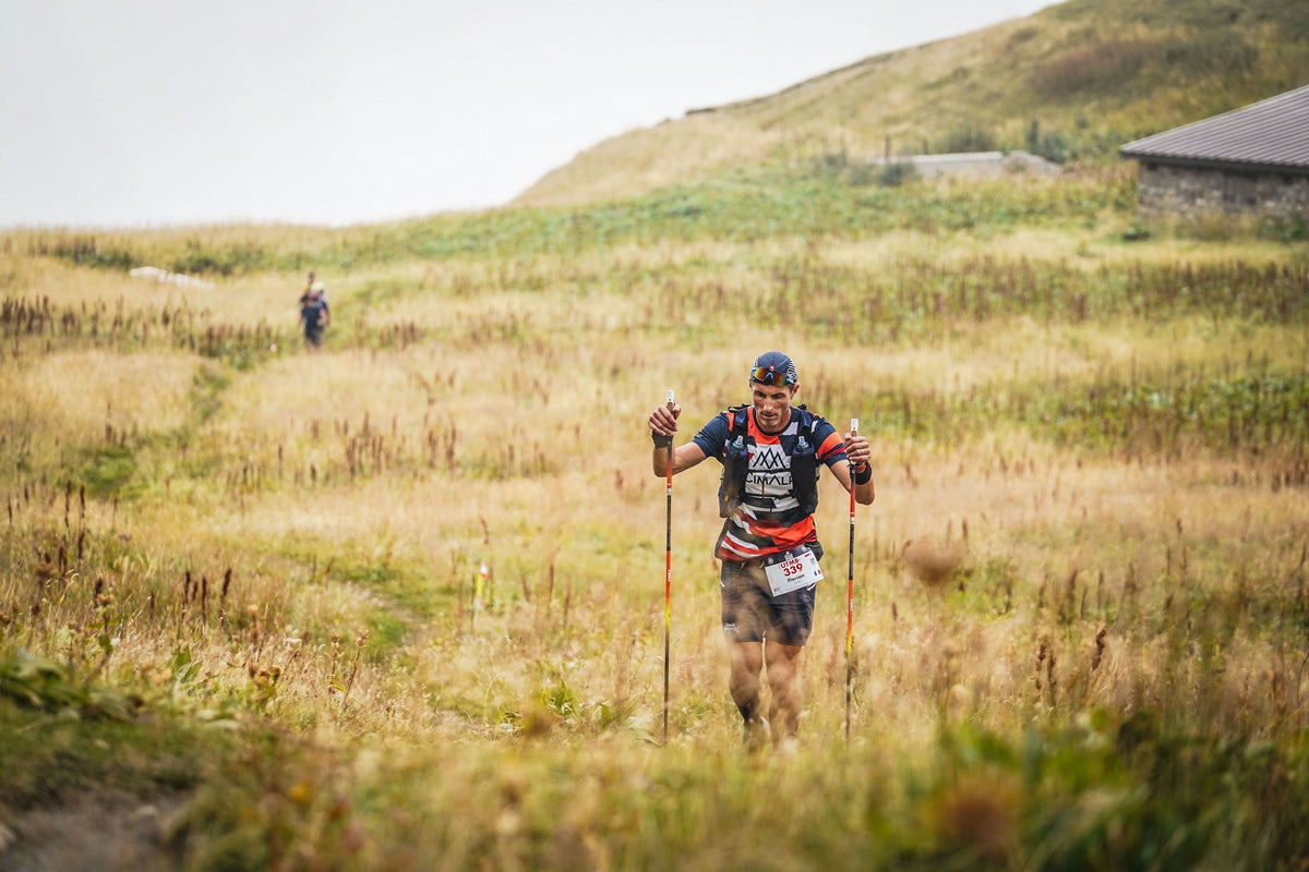 Coureur de l'UTMB avec bâtons progressant dans une prairie d'altitude