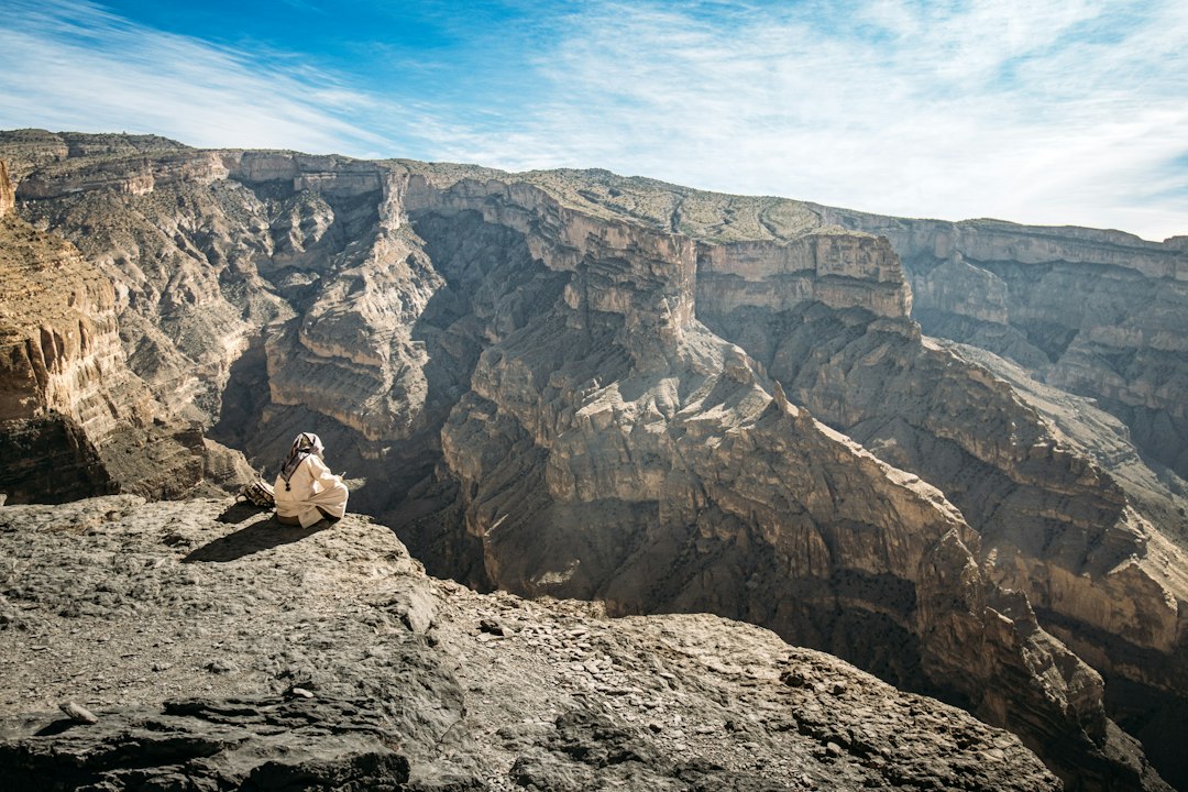Randonneur en vêtement traditionnel au bord du canyon du Wadi Ghul, Jebel Shams, Oman