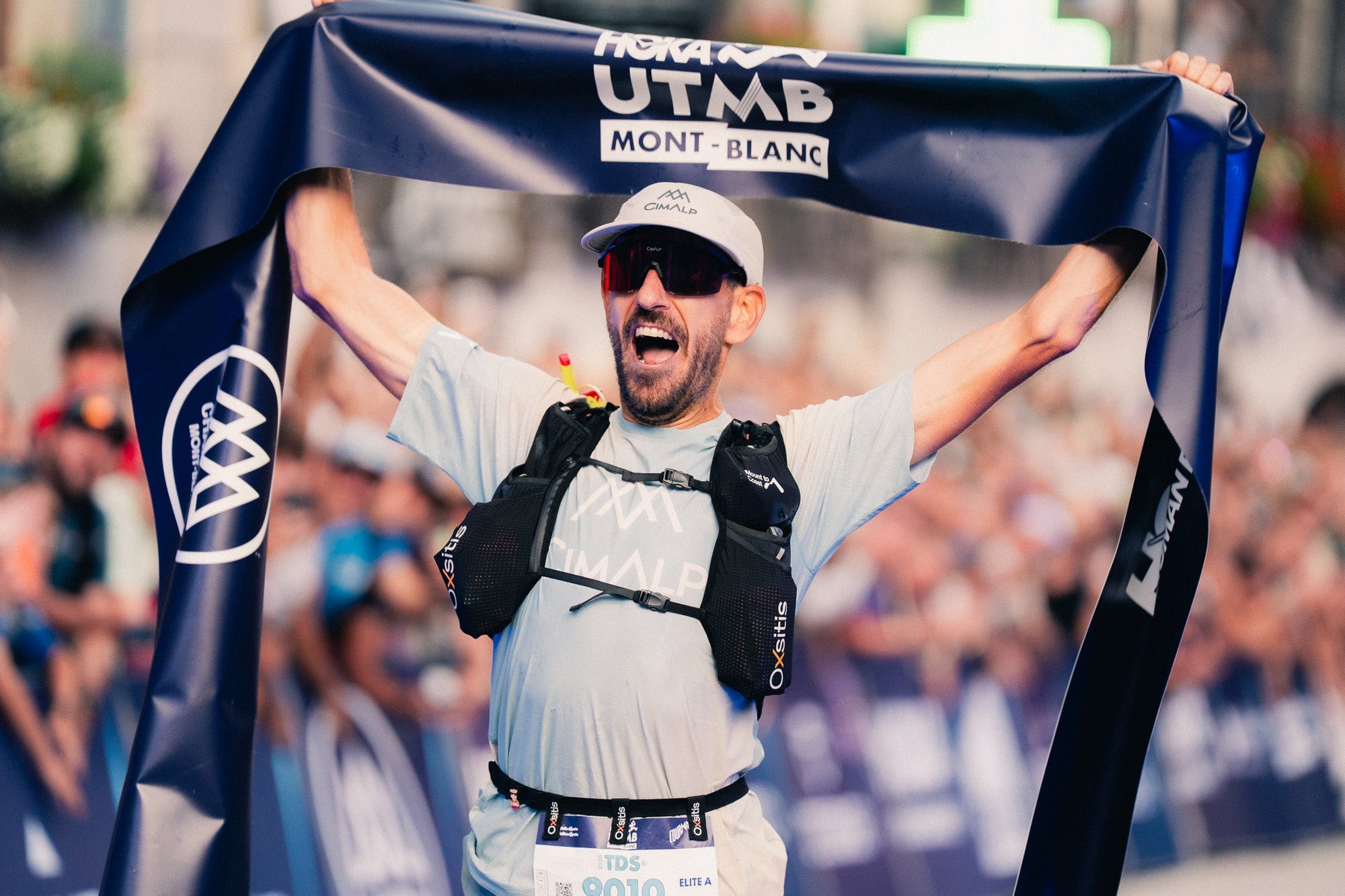 Rémy Brassac brandit la banderole d'arrivée HOKA UTMB Mont-Blanc après sa victoire sur la TDS 2026
